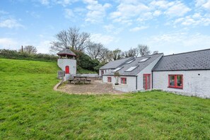 A coastal house with a stone tower, a patio with a table, and a grassy hill. - 3 Bed in Freshwater East (oc-w29240) (Freshwater East)
