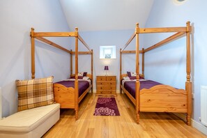 A bedroom with two wooden four-poster beds, a small sofa, and a dresser. - 3 Bed in Freshwater East (oc-w29240) (Freshwater East)