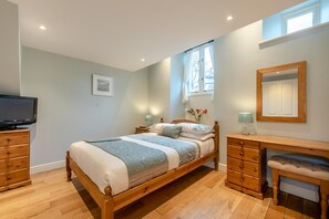 A bedroom with a wooden bed, a TV, a desk, and a mirror. - 3 Bed in Freshwater East (oc-w29240) (Freshwater East)