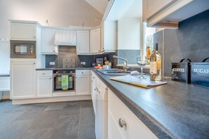 A modern kitchen with white cabinetry, a built-in oven, a microwave, and a coffee and sugar dispenser on the counter. - 3 Bed in Freshwater East (oc-w29240) (Freshwater East)