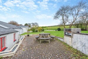 A courtyard with a picnic table, a stone wall, and a building with red windows. - 3 Bed in Freshwater East (oc-w29240) (Freshwater East)