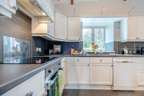 A modern kitchen with white cabinets, a black countertop, a built-in oven, and a window providing natural light. - 3 Bed in Freshwater East (oc-w29240) (Freshwater East)
