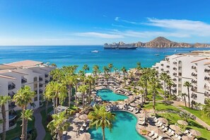 A resort with a pool area, palm trees, and a view of the ocean and ships. - Cabo Beachfront condo for Holidays (Cabo San Lucas)
