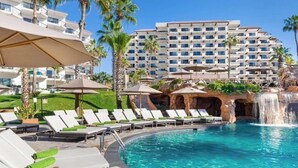 A hotel pool area with lounge chairs, umbrellas, and a waterfall feature. - Cabo Beachfront condo for Holidays (Cabo San Lucas)