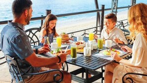 A group of people dining at an outdoor table with a view of the sea and cliffs. - Cabo Beachfront condo for Holidays (Cabo San Lucas)