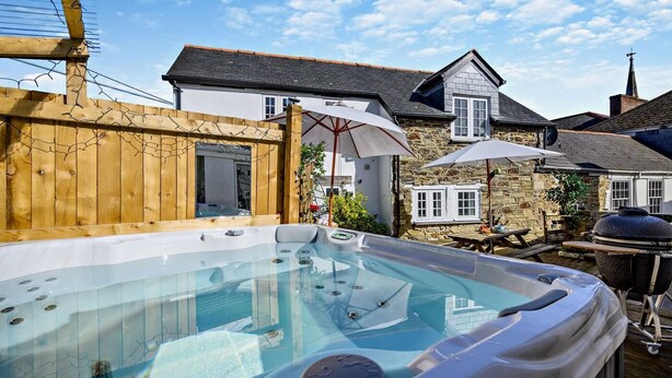 Een hottub in een houten terras, met stenen gebouwen op de achtergrond.