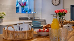 Een ontbijt opstelling met een houten tafel, een mand met bestek, een schaal aardbeien, een fles sinaasappelsap en een vaas bloemen.