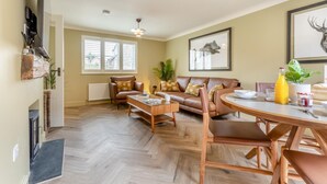 A spacious living room with a fireplace, a dining area with a round table, and a large window with blinds. - 2 Bed in Holt (oc-f29274) (Holt)