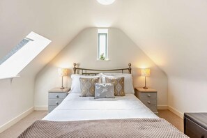 A bedroom with a sloped ceiling, a skylight, a bed with white bedding, two bedside tables with lamps, and a small window.