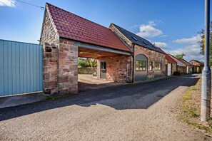 A row of stone buildings with red-tiled roofs, a gravel driveway, and a metal fence.