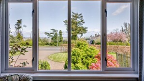 Janela com vista para um jardim bem cuidado, área pavimentada e edifícios ao longe.