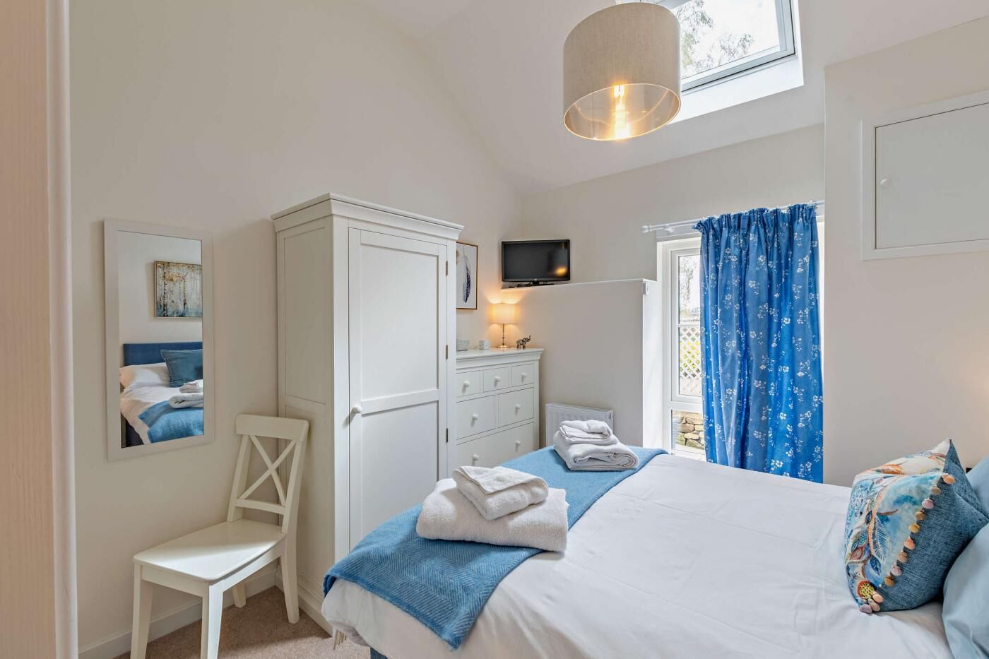 A bedroom with a bed, a desk, a chair, a wardrobe, a TV, and a window with curtains.