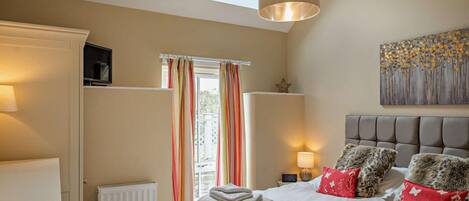 A bedroom with a bed, a radiator, a television, a window with curtains, a ceiling light, and a wall art piece.