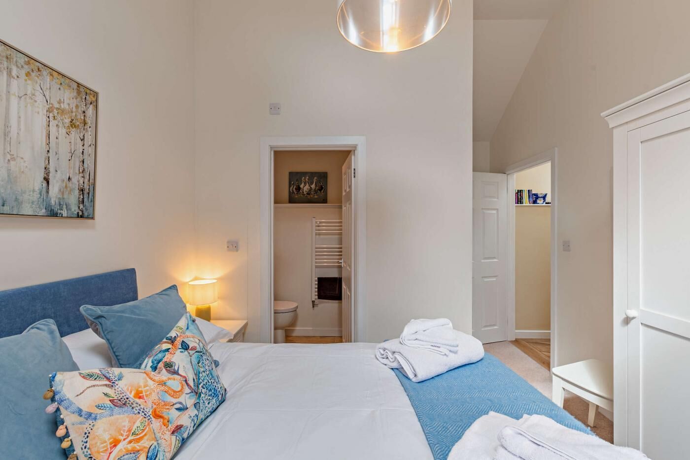 Una camera da letto con un letto, un comodino, una lampada, un armadio e un bagno visibile attraverso una porta aperta.