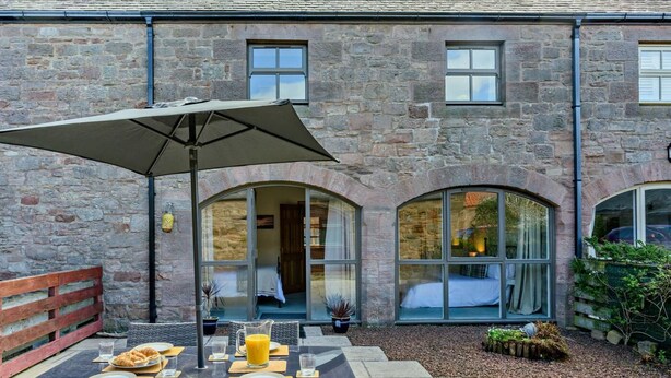 Ein Steinhaus mit Terrasse, komplett mit Tisch, Stühlen und Sonnenschirm.
