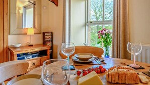 Ein Esstisch mit Brot, Tomaten und Weingläsern, in einem Raum mit Fenster und Spiegel.