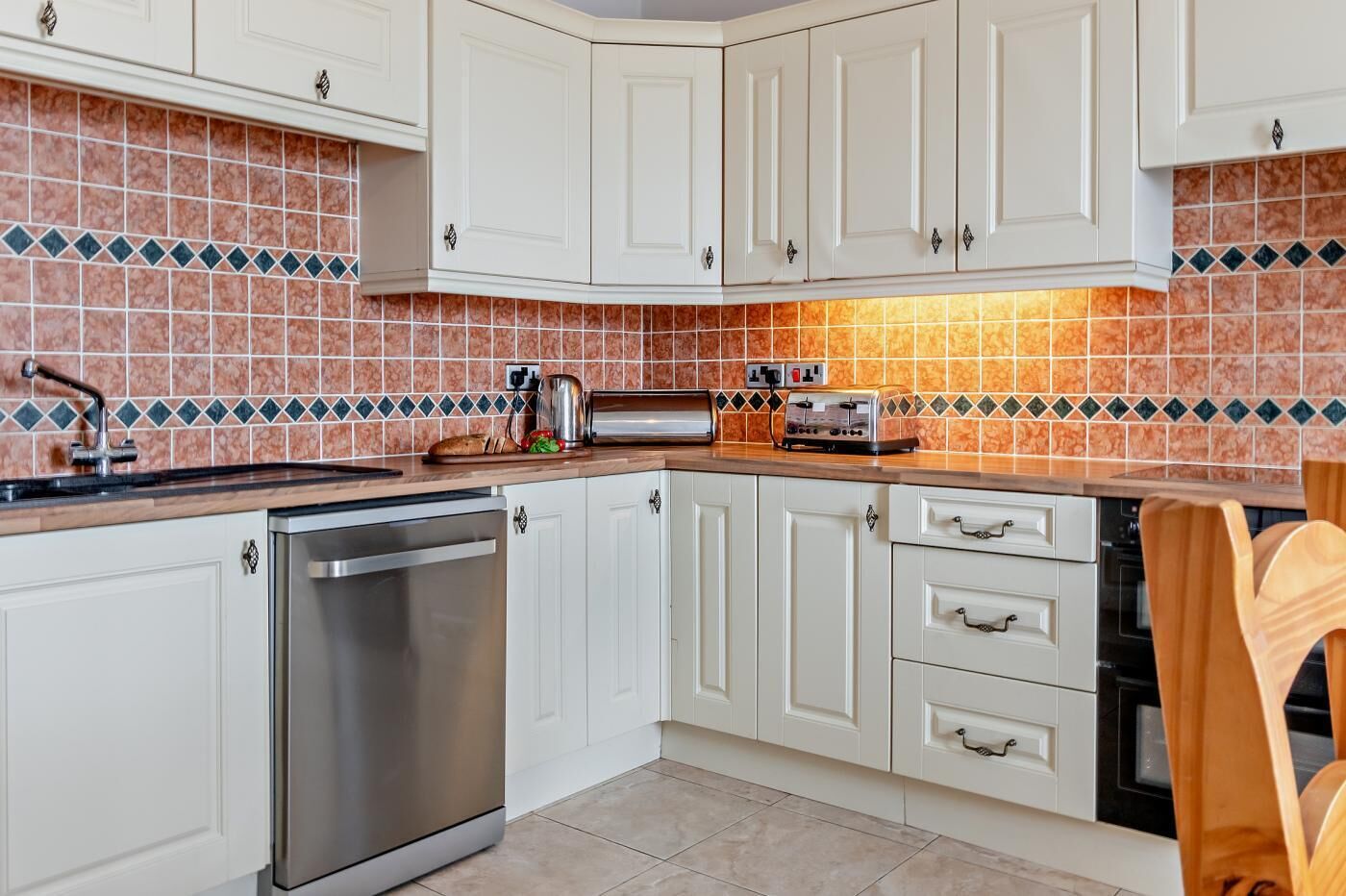 Uma cozinha com armários brancos, lava-louças de aço inoxidável, torradeira e painel de azulejos.