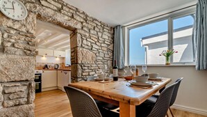 Ein Essbereich mit einer Steinwand, einem Holztisch und Stühlen. Im Hintergrund ist eine Küche zu sehen.