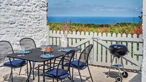 Eine Außenpatio mit einem für vier Personen gedeckten Tisch, einem Grill und Blick aufs Meer.