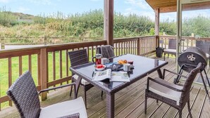 Eine überdachte Terrasse im Freien mit Korbmöbeln, einem Grill und einem Tisch, der mit Speisen und Getränken gedeckt ist.