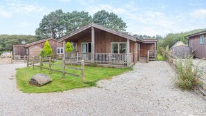 Eine Holzhütte mit Veranda, Kiesweg und umliegenden Bäumen.