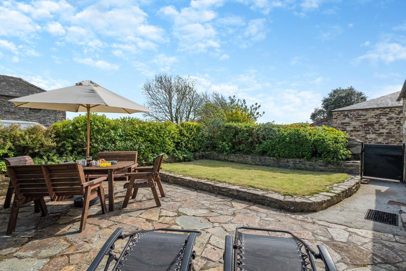 A patio with stone flooring, a wooden table with chairs, and a large umbrella.