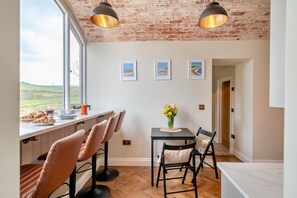 A modern kitchen with a large window, a dining area with a table and chairs, and a brick ceiling. - 2 Bed in Askerswell (oc-t29236) (Askerswell)