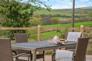 A table set outdoors with wicker chairs, a teapot, glasses, and a tray with pastries. - 2 Bed in Askerswell (oc-t29236) (Askerswell)
