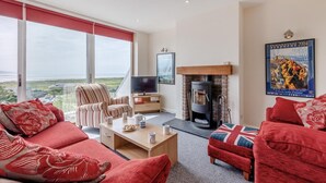 A spacious living room with a large window, a fireplace, and a television. - 3 Bed in Aberdovey (oc-v29263) (Aberdovey)