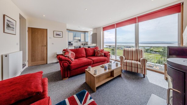 A modern living room with a red sofa, a striped armchair, and a view of the outdoors. - 3 Bed in Aberdovey (oc-v29263) (Aberdovey)