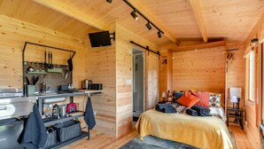 A wooden cabin interior with a kitchen, a bed with colorful pillows, and a small table by the window. - 1 Bed in Cilycwm (oc-t29297) (Cilycwm)