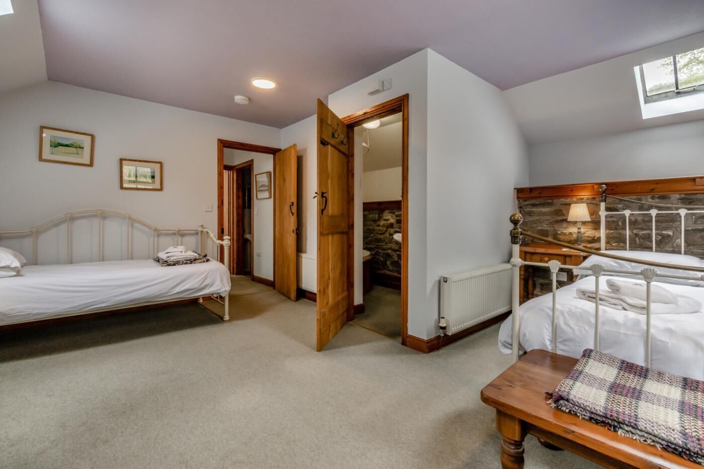A bedroom with two beds, a wooden table, and a stone wall.