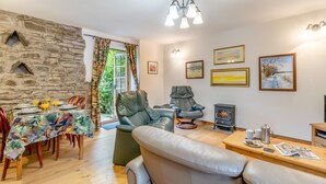 A cozy living room with a stone wall, a dining area with a table set for two, and a fireplace. - 2 Bed in Knighton (oc-t29330) (Felindre)