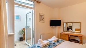 A hotel room with a bed, a desk, a television, a mirror, and a sliding glass door leading to an outdoor area. - 1 Bed in St. Ives (oc-l29205) (St Ives)