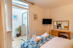 Une chambre d’hôtel équipée d’un lit, d’un bureau, d’une télévision, d’un miroir et d’une porte-fenêtre coulissante donnant sur un espace extérieur.
