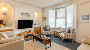 A living room with a television, two plaid armchairs, a coffee table, and a large window with blinds. - 1 Bed in St. Ives (oc-l29205) (St Ives)