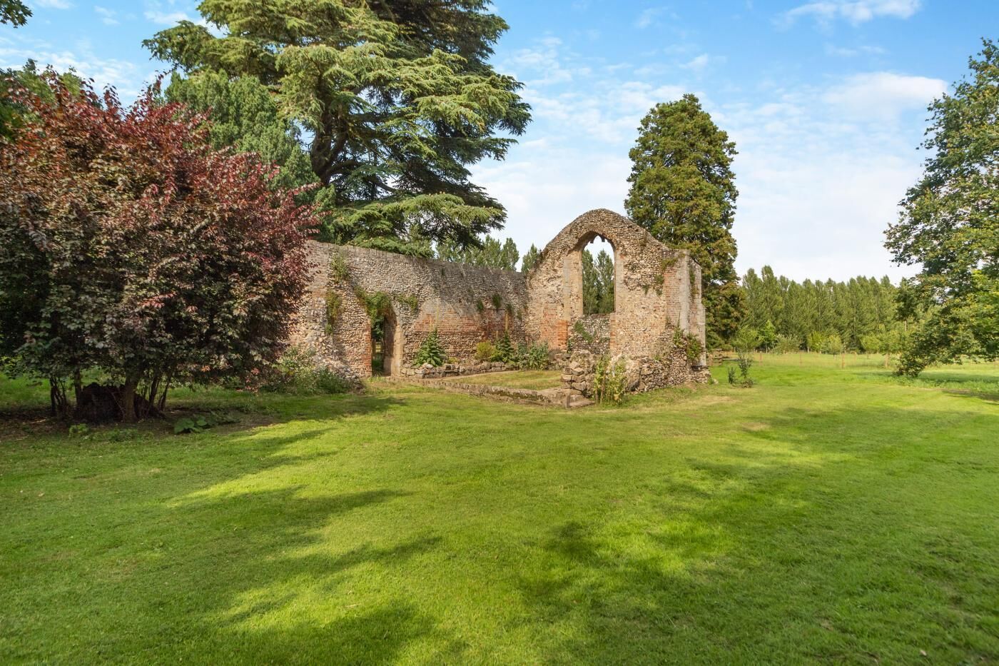 An ancient stone structure with arched openings, surrounded by a well-maintained grassy area and mature trees.