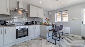 A modern kitchen with white cabinets, a stone backsplash, a built-in oven, and a window with blinds. - 2 Bed in Oxborough (oc-r29291) (Oxborough)