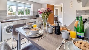 A modern kitchen with a dining area, a washing machine, breakfast items, and a view of the outdoors. - 2 Bed in Oxborough (oc-r29291) (Oxborough)