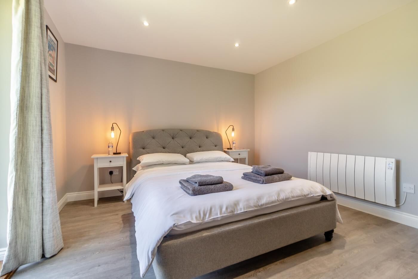 Ein Schlafzimmer mit einem großen Bett, Nachttischen, einem Heizkörper und einem Bild an der Wand.