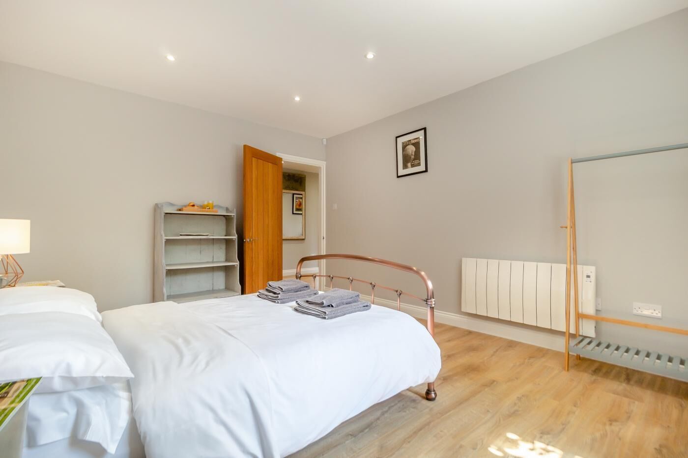 Une chambre à coucher comprenant un lit, une table de chevet, une armoire, un radiateur et une porte donnant sur une autre pièce.