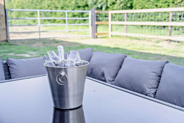 A metal bucket with glasses on a table in an outdoor setting.