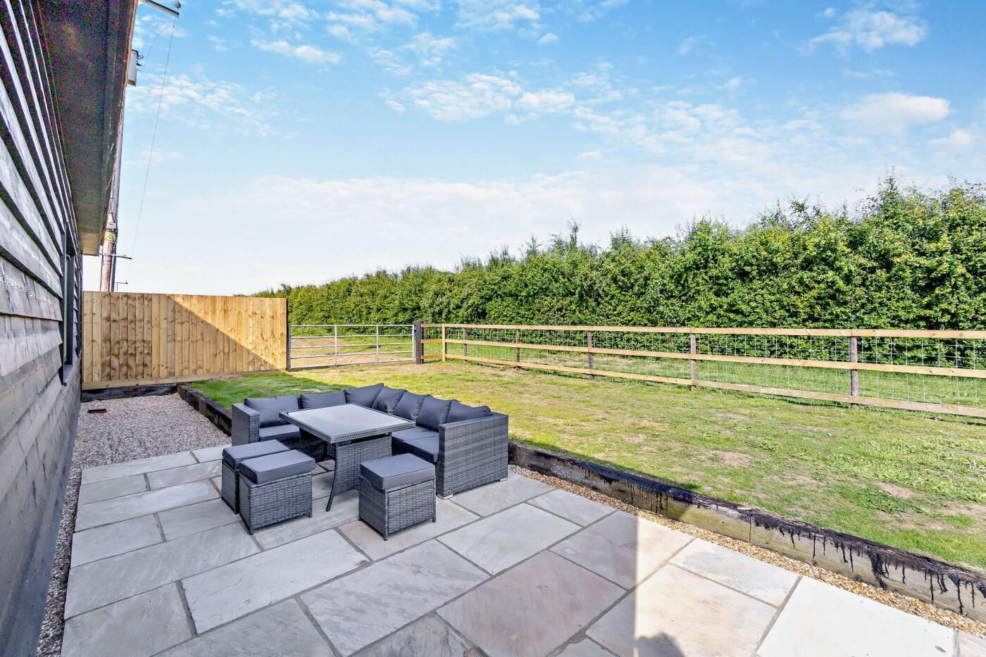 Une terrasse extérieure avec un espace salon, un sol en pierre et une clôture en bois.