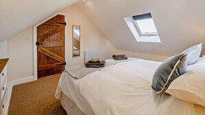 A bedroom with a sloped ceiling, a skylight, a bed with pillows, a bedside table, and a wooden door. - 2 Bed in Feering (oc-p29293) (Feering)