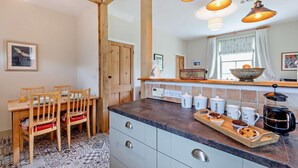 Une cuisine avec une table à manger en bois, des chaises, une machine à café et des récipients étiquetés pour le café, le thé et le sucre.