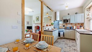 Une cuisine moderne avec un coin repas, comprenant une table en bois dressée pour le petit-déjeuner, un four encastré et un four à micro-ondes.