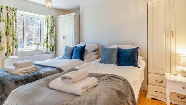 A bedroom with two beds, a window with curtains, a chandelier, and a wardrobe. - 2 Bed in Holt (oc-m29326) (Holt)