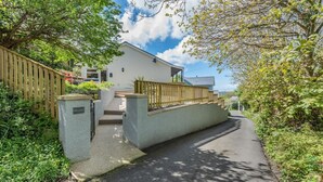 Een woonhuis met een verharde oprit, een houten hek en een wit gebouw met balkon.