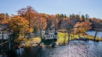 A two-story house with a gabled roof, surrounded by autumn foliage and a body of water.