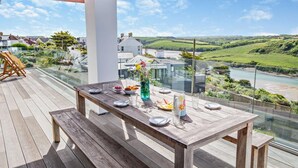 Une terrasse en bois avec une table dressée pour le repas, offrant une vue sur une rivière et un paysage verdoyant.